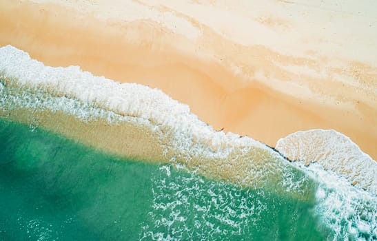 Aerial top down view of turquoise ocean wave reaching the coastline.