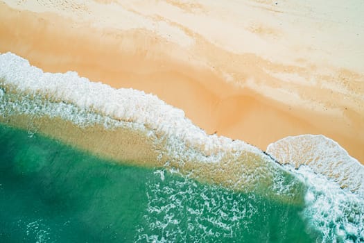 Aerial top down view of turquoise ocean wave reaching the coastline.