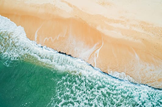 Aerial top down view of turquoise ocean wave reaching the coastline.