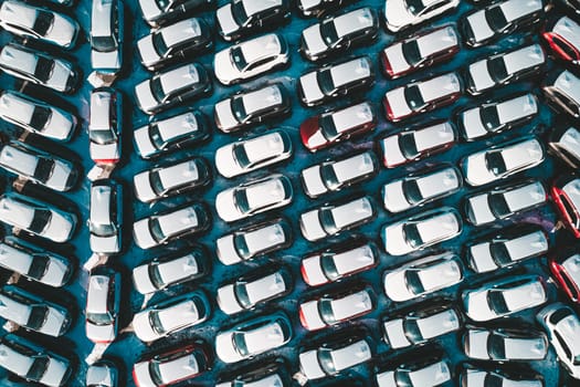 Aerial top down view of new cars parked in car parking lot. Car dealer parking lot full of new automobiles. New cars lined up for import and export business.