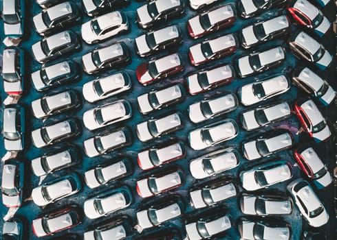 Aerial top down view of new cars parked in car parking lot. Car dealer parking lot full of new automobiles. New cars lined up for import and export business.