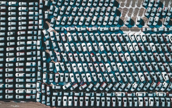 Aerial top down view of new cars parked in car parking lot. Car dealer parking lot full of new automobiles. New cars lined up for import and export business.