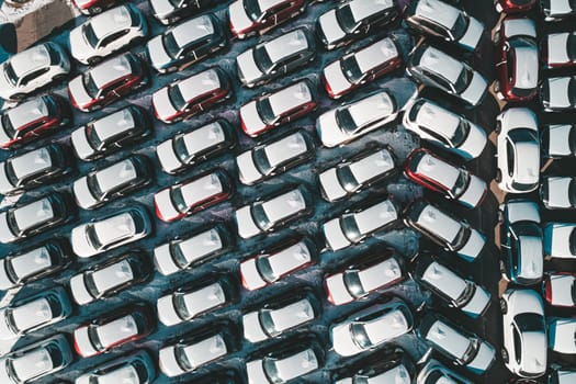 Aerial top down view of new cars parked in car parking lot. Car dealer parking lot full of new automobiles. New cars lined up for import and export business.