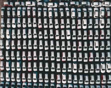 Aerial top down view of new cars parked in car parking lot. Car dealer parking lot full of new automobiles. New cars lined up for import and export business.