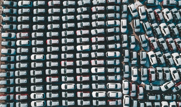 Aerial top down view of new cars parked in car parking lot. Car dealer parking lot full of new automobiles. New cars lined up for import and export business.