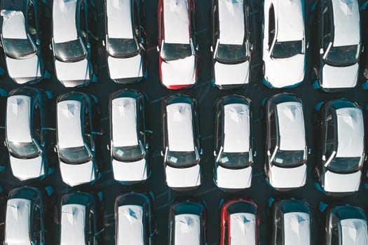 Aerial top down view of new cars parked in car parking lot. Car dealer parking lot full of new automobiles. New cars lined up for import and export business.