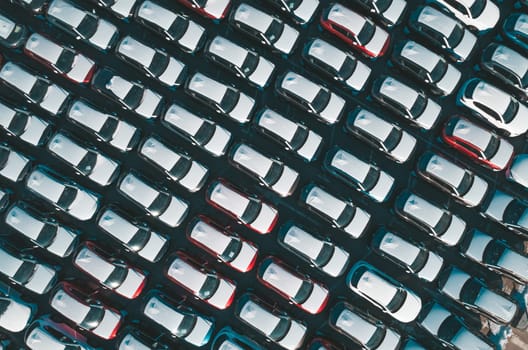 Aerial top down view of new cars parked in car parking lot. Car dealer parking lot full of new automobiles. New cars lined up for import and export business.