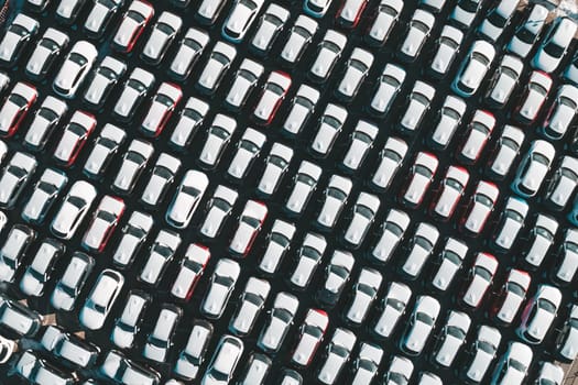 Aerial top down view of new cars parked in car parking lot. Car dealer parking lot full of new automobiles. New cars lined up for import and export business.