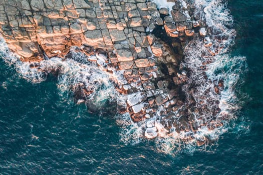 Aerial top down view of an ocean blue waves breaking on the rocks