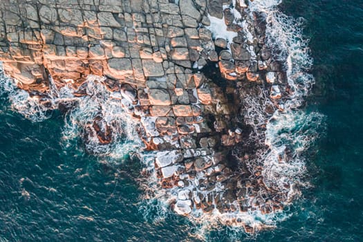 Aerial top down view of an ocean blue waves breaking on the rocks