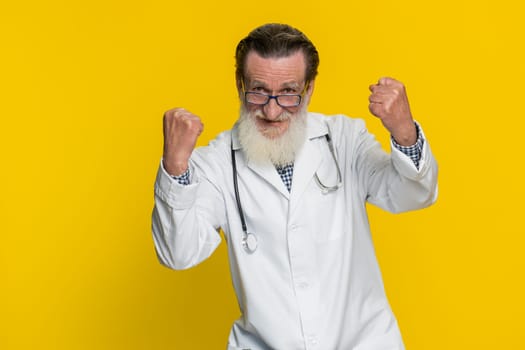 Senior doctor cardiologist old man celebrating success victory, winning, achievement, good positive news, triumph, succeed. Apothecary pharmacy grandfather champion isolated on yellow background