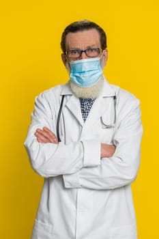 Happy senior doctor cardiologist man removing taking off medical protective mask. Flu treatment cure. Ending of pandemic quarantine. Apothecary pharmacy old grandfather on yellow background. Vertical