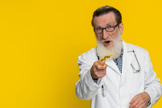 Magician wizard senior excited doctor cardiologist man with magic wand making wish come true, casting magician spell, health cure treatment help. Apothecary pharmacy grandfather on yellow background