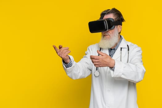 Excited senior doctor cardiologist man using headset helmet app watching virtual reality 3D 360 video. Apothecary grandfather in VR goggles on yellow background. Future medicine technology. Copy-space