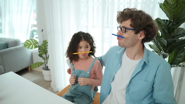 Funny caucasian dad and american kid doing funny face while put pencil between lip and nose. Cute family study about writing engineering prompt together and generating AI at laptop on table. Pedagogy.