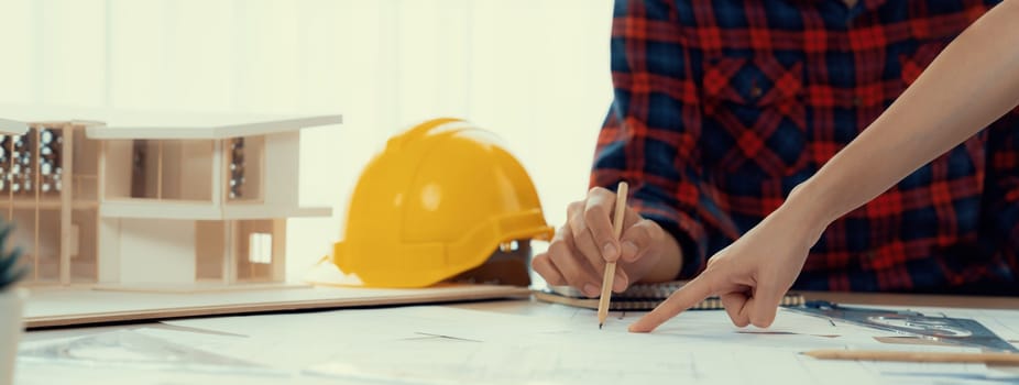 Cropped image of cooperative architect team decide and work together on meeting table with house model, safety helmet and architectural plan scatter around. Closeup. Focus on hand. Burgeoning.