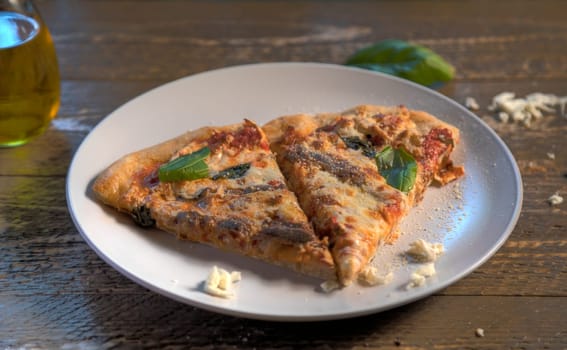 Side view of anchovy pizza on natural wood surface.