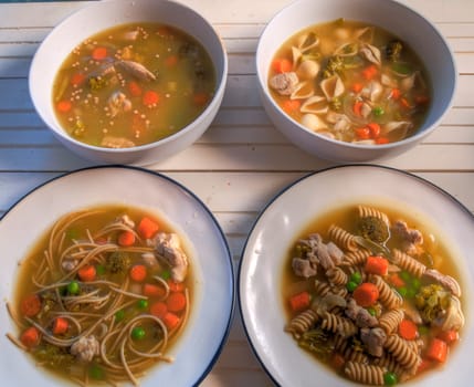 Top view of four chicken noodle types on natural wood surface