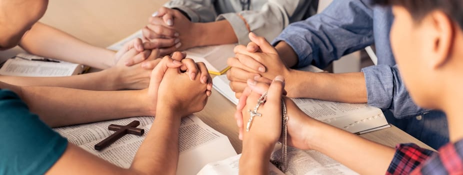 Cropped image of diversity people hand praying together at wooden church on bible book while hold hand together with believe. Concept of hope, religion, faith, god blessing concept. Burgeoning.