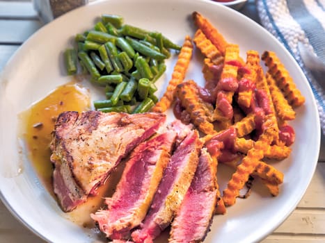 Top View of grilled tuna steak with sweet potato fries and green beans