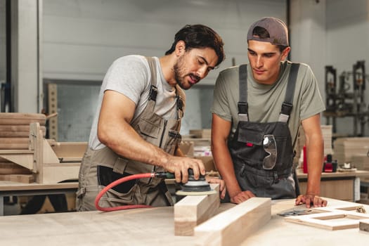 Two young carpenters working with wood standing at table in workshop close up