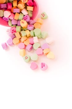 Conversation heart candies spilled from pink bucket.