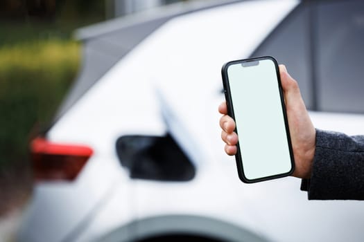 Process of charging is showing on smartphone. Close up view of man with his electric car. Man holding smartphone while charging car at electric vehicle charging station, closeup.