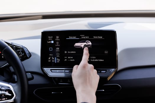 Male finger using an intelligent multimedia touchscreen system for modern electric automobiles. Green energy, zero-emission car interior view. Long-range electric vehicle.