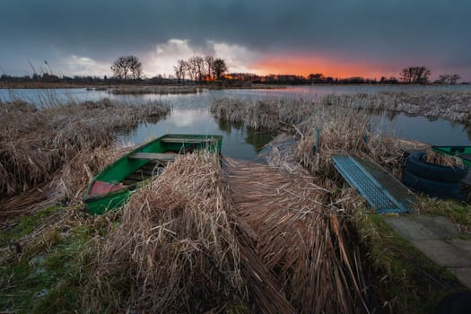 Moored boat in the reeds on the shore of the lake, view during sunset, eastern Poland