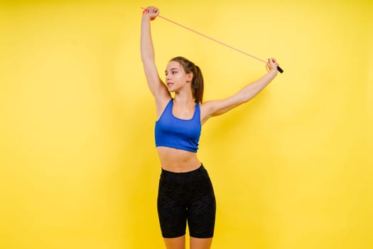 Portrait of gentle muscular woman holding skipping rope on her neck over yellow background