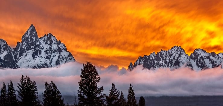 A setting sun and a bank of fog surround the Grand Tetons at Grand Teton National Park, Wyoming