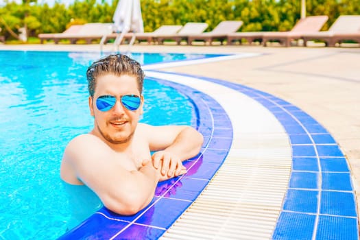 A man looks out of the pool, hanging on the railing. Young man having a good time in the swimming pool.