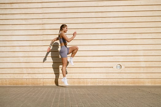 Young fit woman in sportswear leaping in the air with wall backdrop outdoors. High quality photo