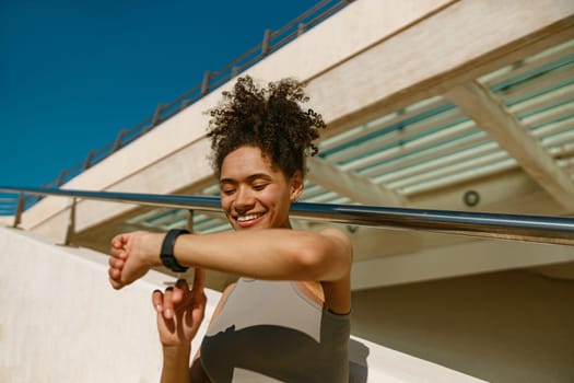 Young woman in sportswear looking on smartwatch before exercising. Outdoor sports in the morning