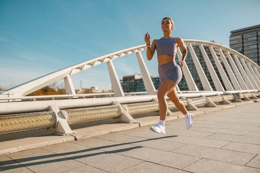 Active woman athlete running along an outdoor track on modern buildings background