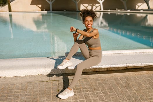 Young woman in sportswear looking on smartwatch before exercising. Outdoor sports in the morning