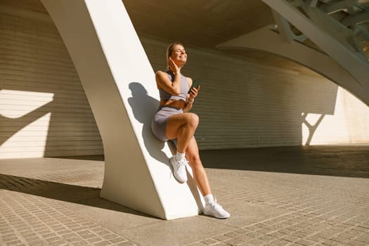 Smiling woman in sportswear have a rest after workout outside standing on bridge background