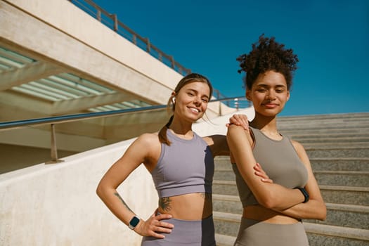 Smiling female sportswomen have a rest after morning jogging outdoors and looks camera