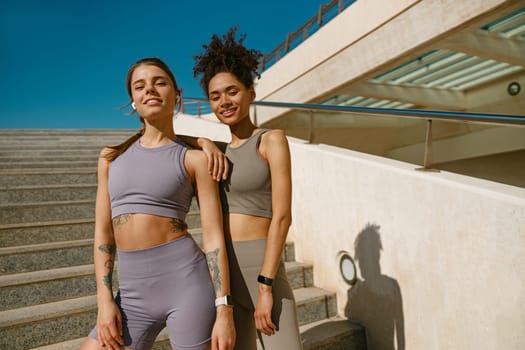 Smiling female sportswomen have a rest after morning jogging outdoors and looks camera