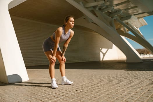 Fit woman in sportswear have a rest after workout outside standing on building background