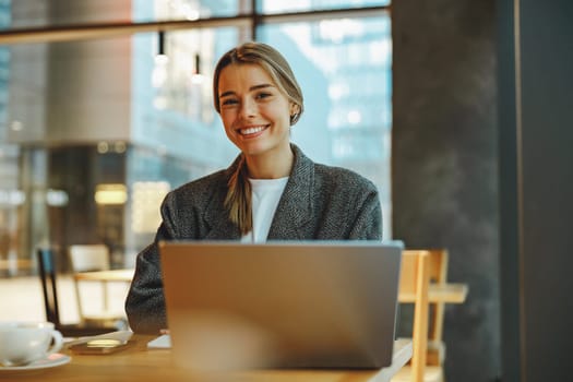 Smiling woman manager working on laptop while sitting in cozy cafe. High quality photo