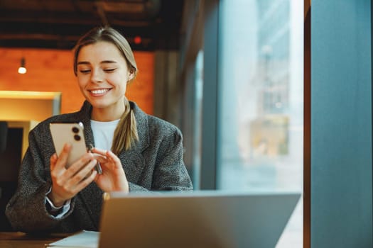 Smiling woman manager is using phone and work on laptop outside of office. Distance work concept