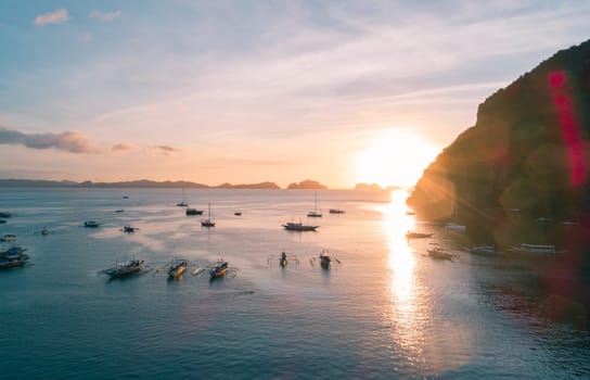 Aerial view of cliffs in the sea, yachts are sailing nearby, mountains covered with tropical forest. Aerial view of the gorgeous tropical mountains and the ocean.