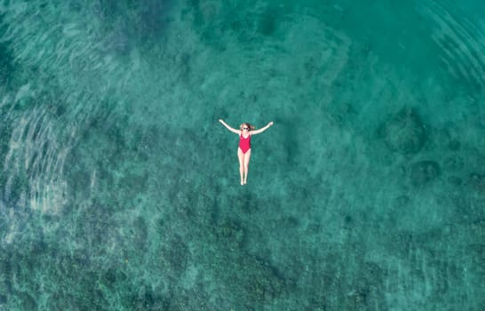 Aerial View of a Woman in Red Swimsuit Floating Serenely on the Crystal Clear Ocean Waters During Midday