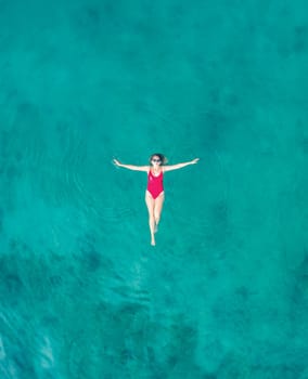 Aerial View of a Woman in Red Swimsuit Floating Serenely on the Crystal Clear Ocean Waters During Midday