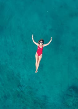 Aerial View of a Woman in Red Swimsuit Floating Serenely on the Crystal Clear Ocean Waters During Midday