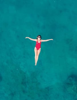 Aerial View of a Woman in Red Swimsuit Floating Serenely on the Crystal Clear Ocean Waters During Midday