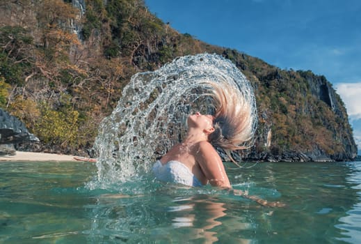 Woman Flipping Her Hair in Clear Waters Near a Rocky Cliff on a Sunny Day