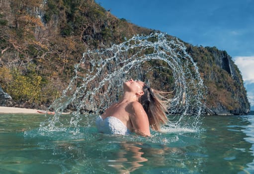 Woman Flipping Her Hair in Clear Waters Near a Rocky Cliff on a Sunny Day