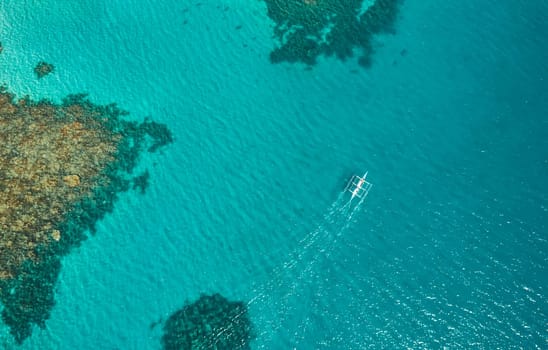 Aerial top view of Banca boat floating in open sea with clear and turquoise water on sunny day . Tropical landscape.